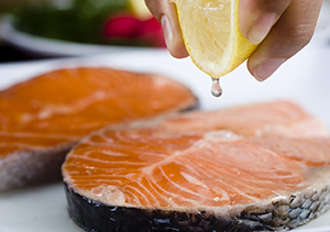 Primer plano de una mano que exprime limón sobre un filete de salmón.